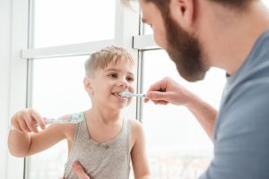 father helping son brush teeth